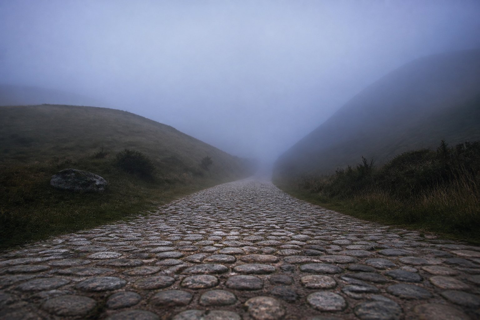 Illustration : une route pav&eacute;e qui s&rsquo;enfonce dans une brume bleue entre deux collines rondes.